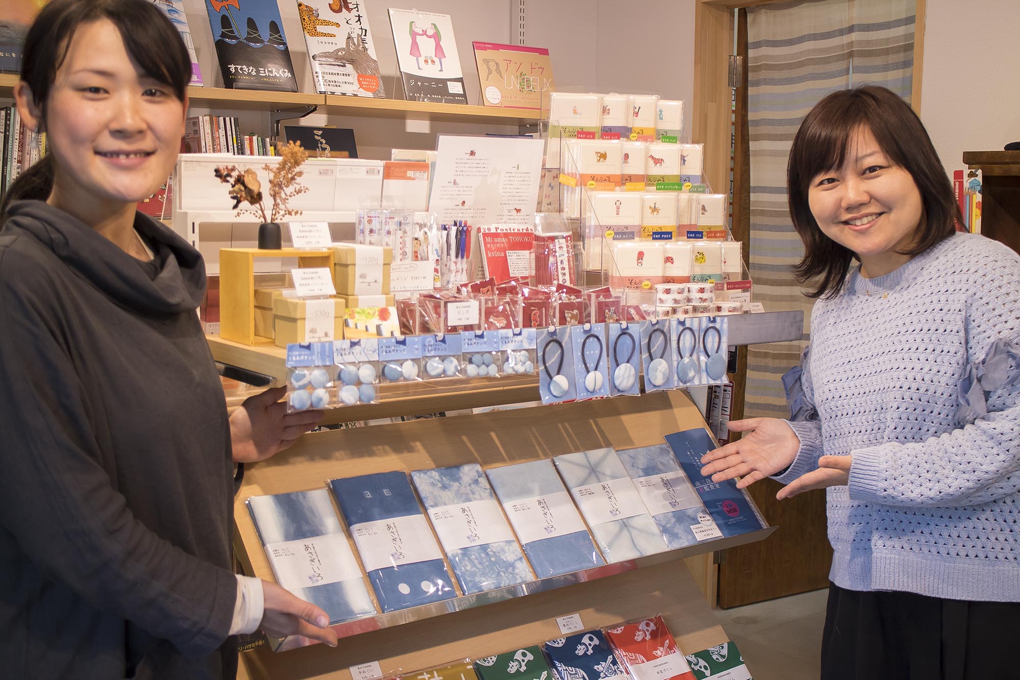 文房具が陳列された商品棚をはさんで、リポーターの女性と中村さんが笑顔で商品を紹介している写真