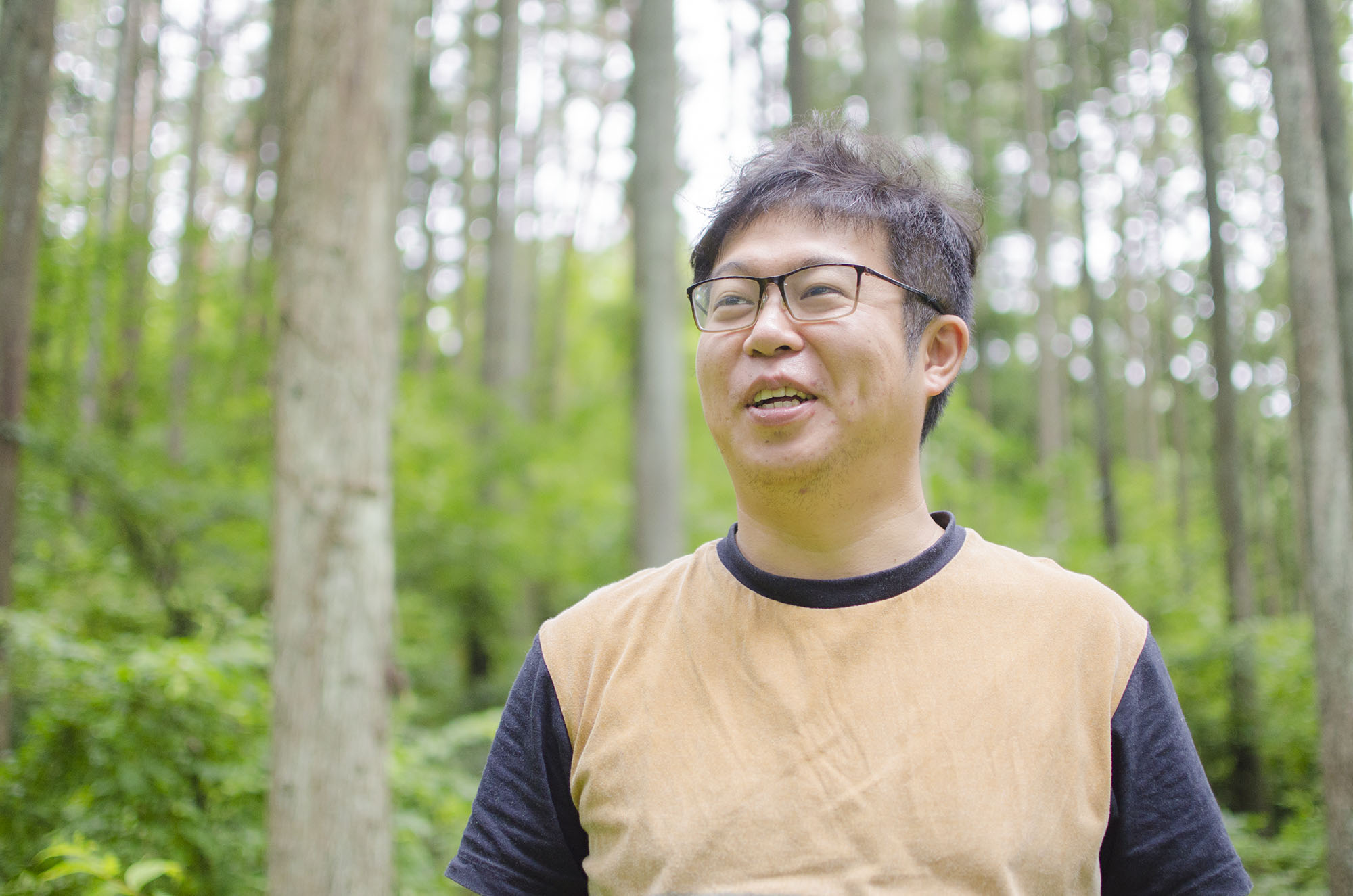 緑の木々が生えた森の中にいる佐藤さんの写真