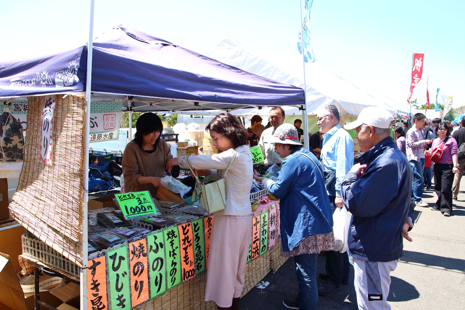値札には「3品で1000円」などと書かれている様々な種類の乾物が並ぶブースに沢山のお客さんが集まり、商品を購入している様子の写真