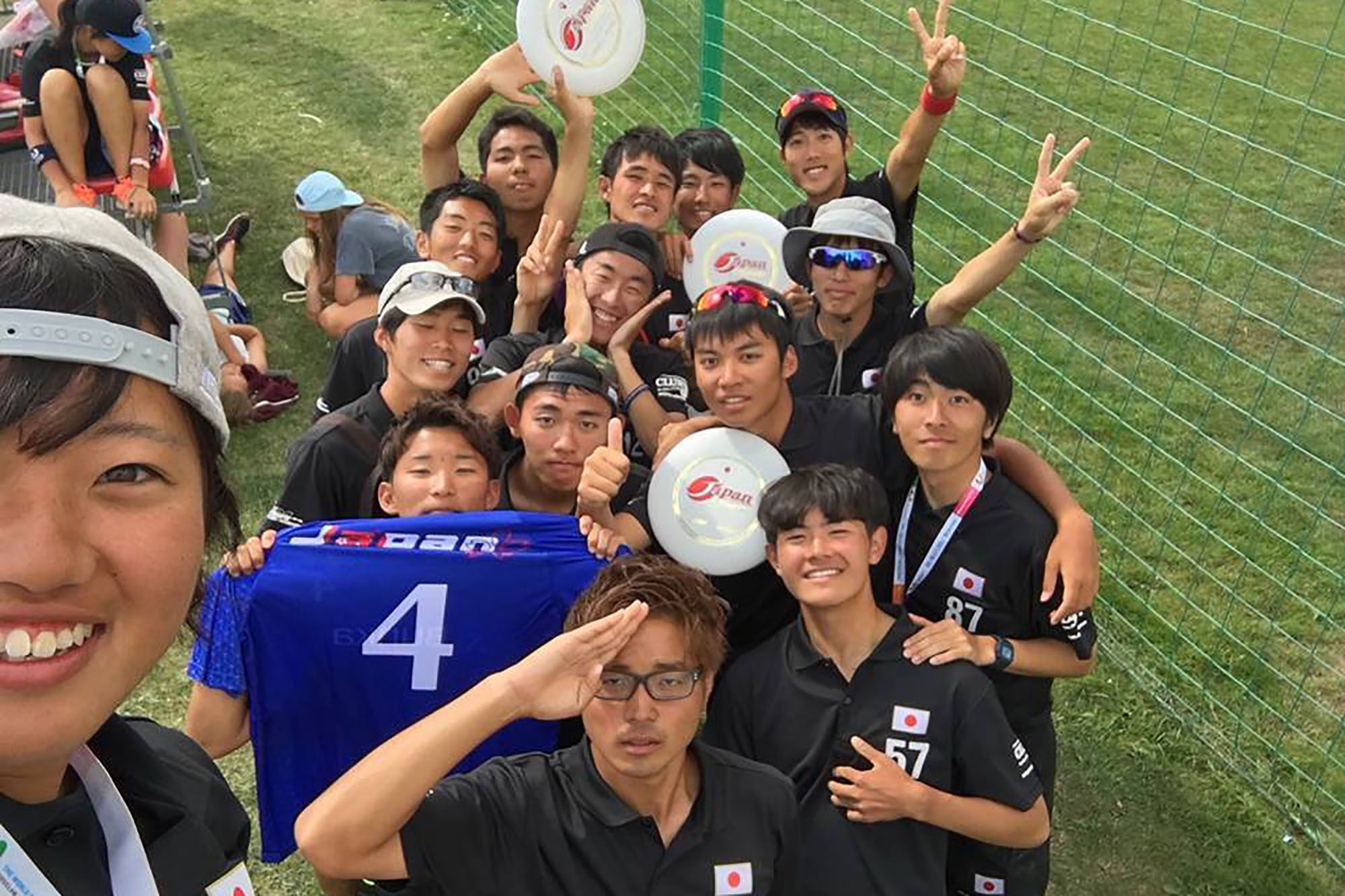 フリスビーを持った日本のユニフォームを着た若者たちが集まり、ピースサインなどをしてカメラに笑顔を見せている写真
