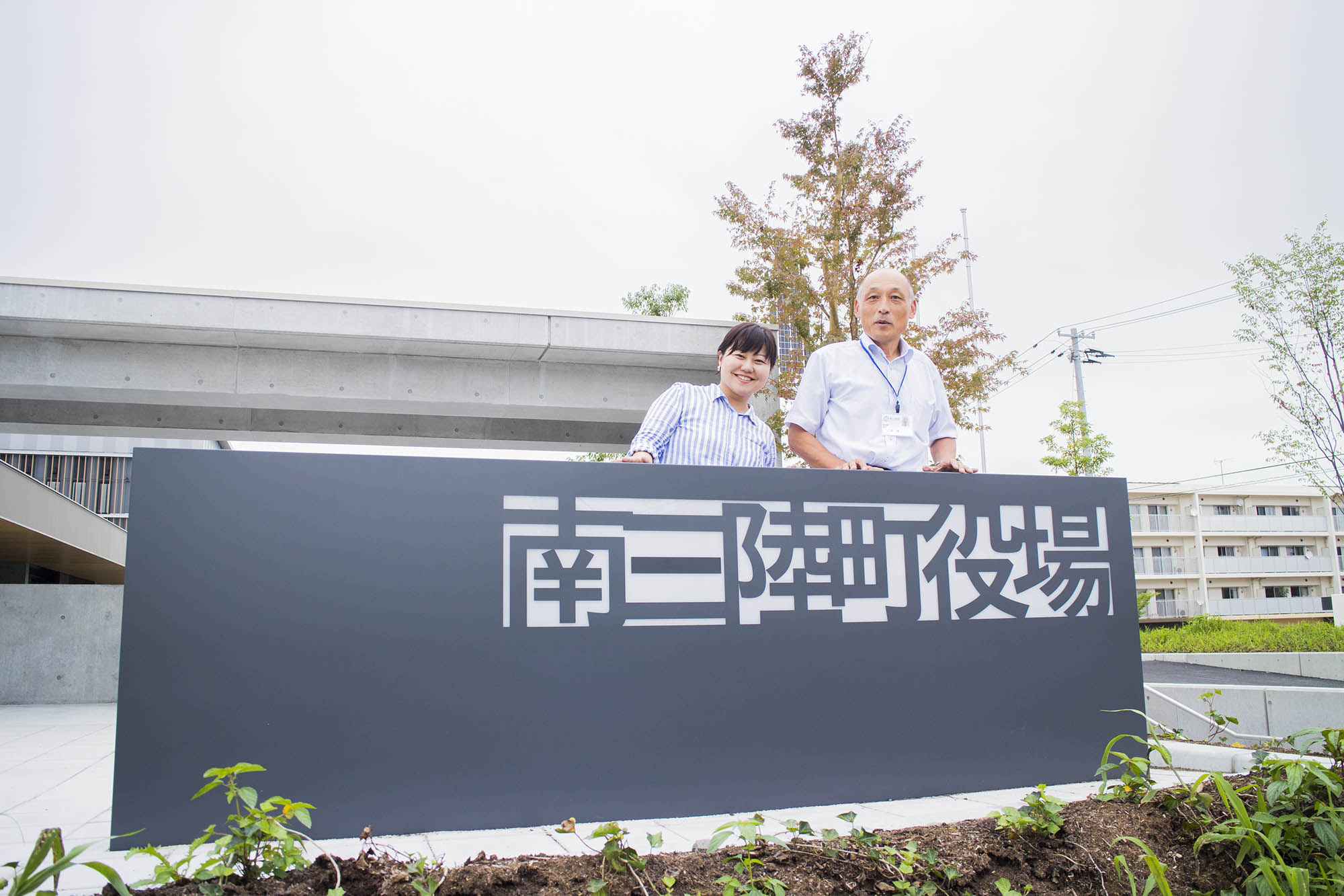 リポーターの女性と三浦さんが「南三陸町役場」の大きな看板の後ろに並び、新庁舎の前で記念撮影している写真