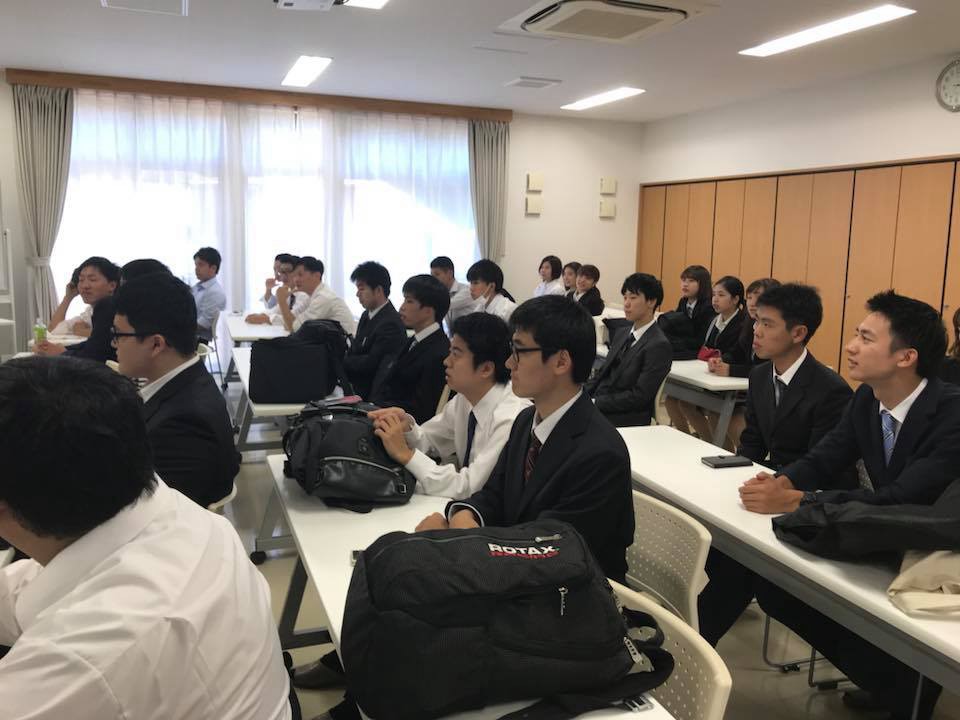 広い室内で多数の学生が整然と机に座り、前方の同じ方向を見ている様子が写っている写真