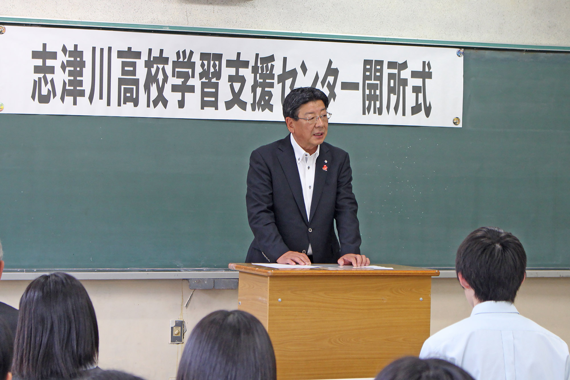 「志津川高校学習支援センター開所式」と書かれた紙が貼られた黒板の前の教壇に佐藤町長が立ち、話をしている様子の写真