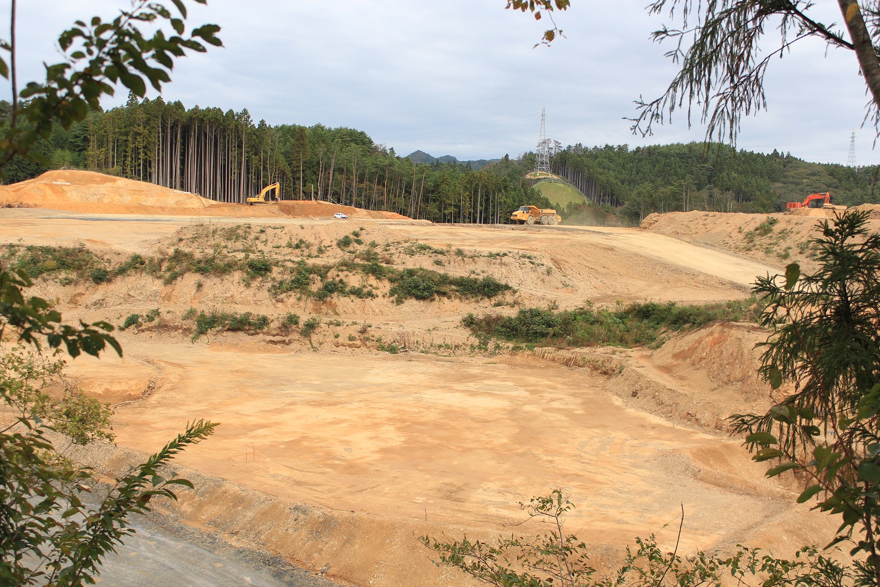 手前に平らにならされた造成地、奥では複数のショベルカーとダンプカーが稼働している様子の写真