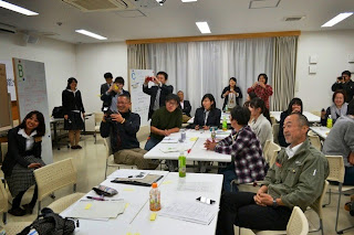 発表を聞いている参加者たちが拍手をしたり写真を撮ったりしながら、楽しそうに全体を見守っている写真