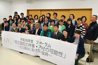 「南三陸町の林業・木材の可能性～人口減少に負けない復興～」と書かれた横断幕を持ち、30人以上の参加者が並んで記念撮影をしている写真