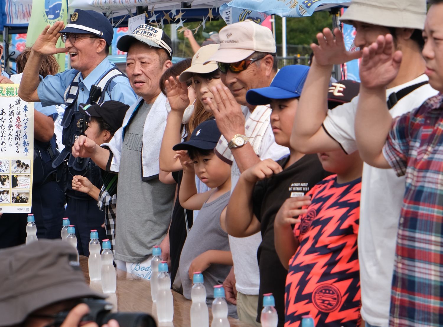 地域の子どもや大人、警察官が並んで一斉に敬礼をしている写真