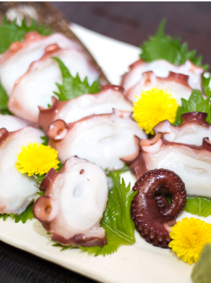 タコの刺身が大葉と菊と一緒に白い皿に盛り付けられている写真