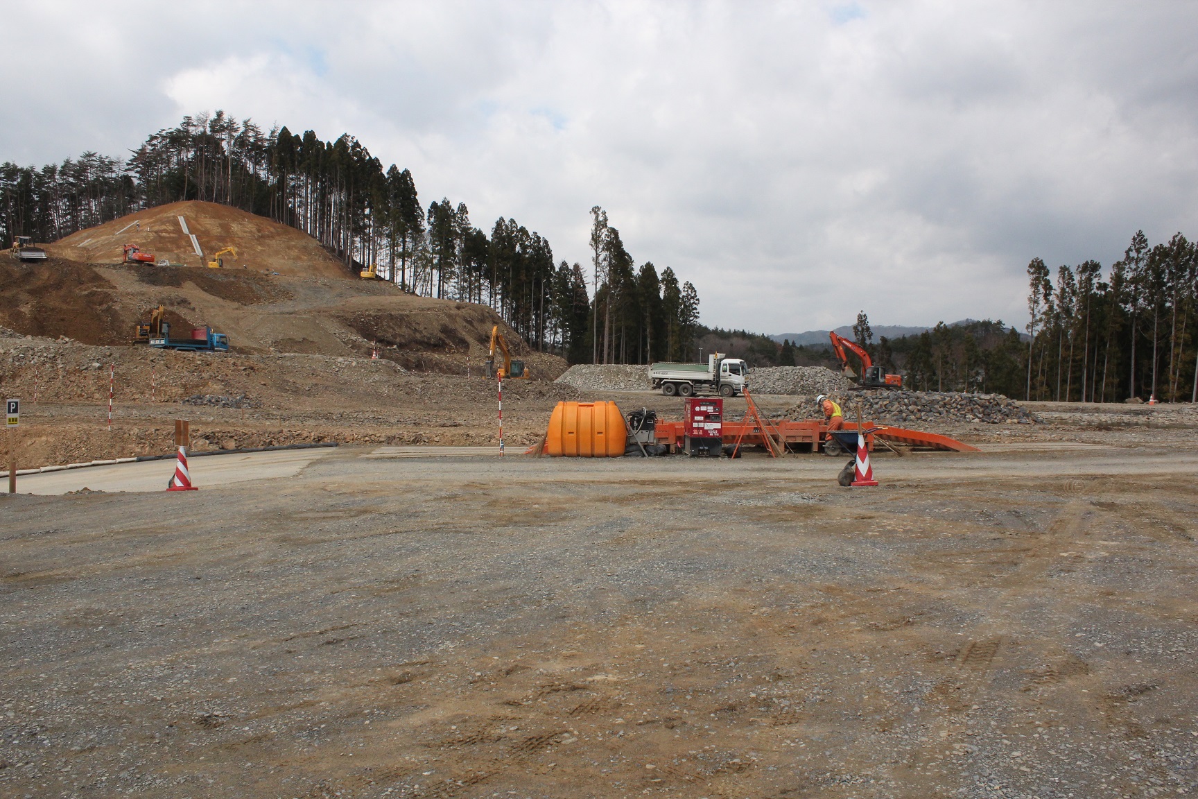 山の斜面が段状に削られ、複数の重機や作業員が整地作業を行う広大な造成現場の様子を写した写真
