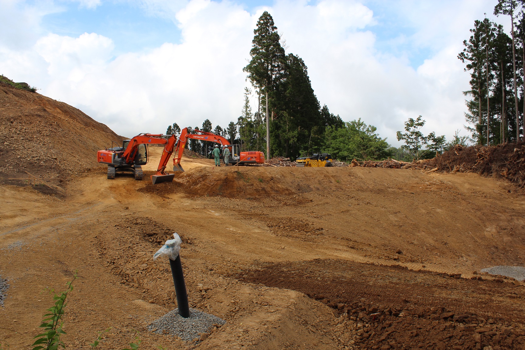 工事現場で重機が整地作業を行っており、作業員がショベルカーの周りに集まっている様子の写真
