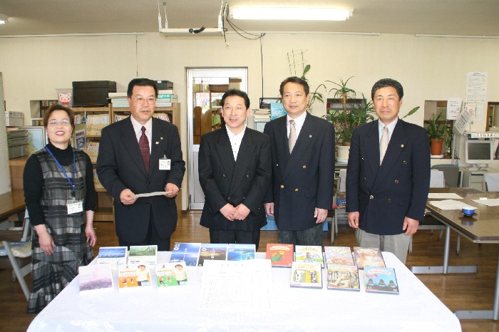寄贈されたDVDが机の上に並べられ、南三陸志津川ライオンズクラブの関係者の方々5名が並び笑顔で写っている記念写真