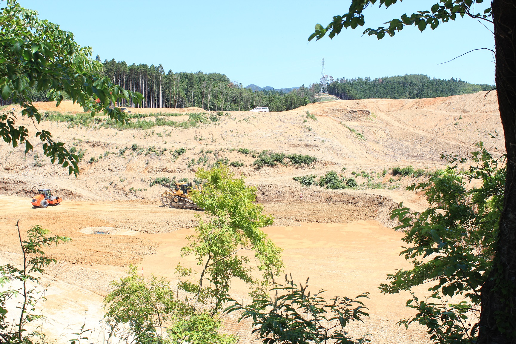 切り開かれた造成地に1台のロードローラーとブルドーザーが見える写真