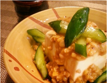 ベージュ色の皿の上に冷ややっこが盛られており、その上に納豆ときゅうりを和えたものがのっている写真