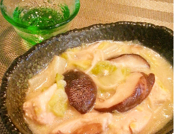 黒い器に大きくカットされた椎茸や白菜、鶏肉などが入ったクリーム風の煮込み料理が盛られ、後ろに緑色のガラスの器が置かれている写真