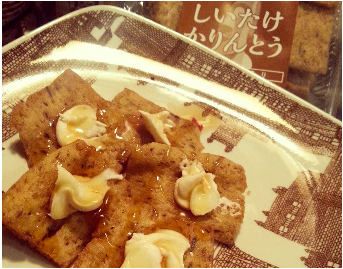 四角くカットされた「しいたけかりんとう」の上にクリームチーズとハチミツがかかっているスイーツが皿に盛られており、背景に商品の袋が見える写真