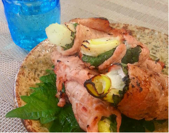 皿の上に大葉を敷き、その上に長ねぎとしその葉で包んで豚肉で巻いて焼いた料理が三つ並び盛り付けられている写真