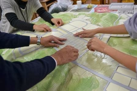 複数の人が模型の上に道路や区画パーツを手で配置しながら街の構成を調整している様子の写真