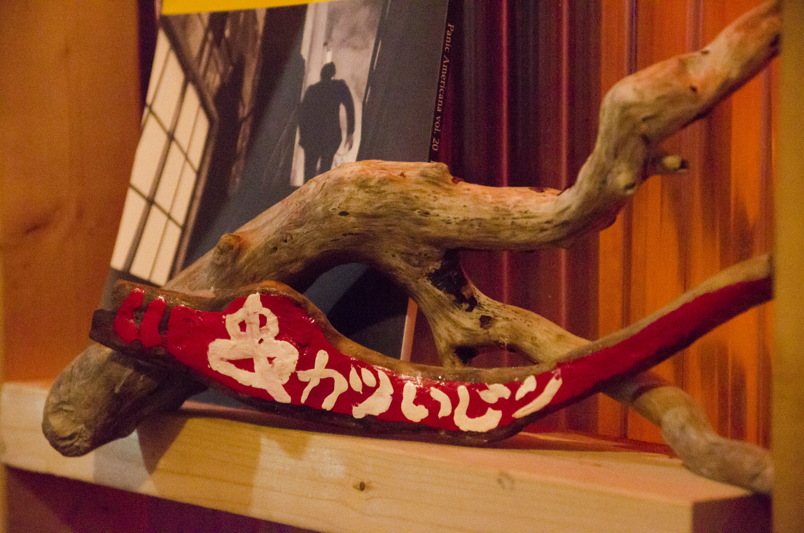 大きな流木の前に、赤く塗られた流木に白いいペイントで「串カツいじり」と手書きされた看板風のオブジェが棚に飾られている写真