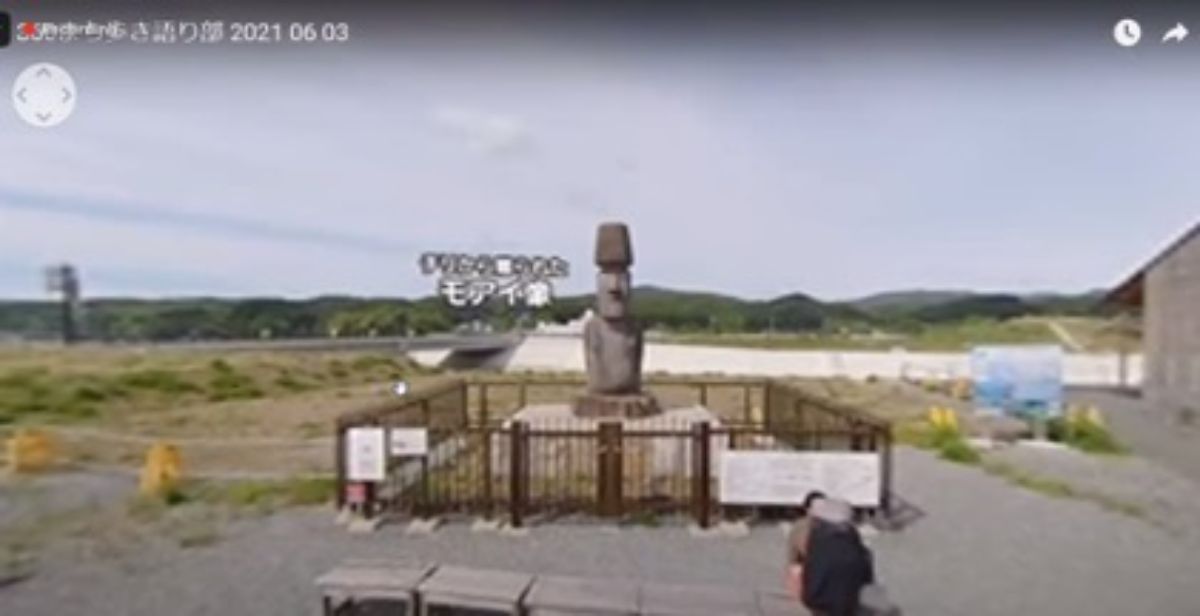 奥には山々が見える屋外の広い空き地の中に、フェンスで囲まれたモアイ像が設置されているスクリーンショット画像