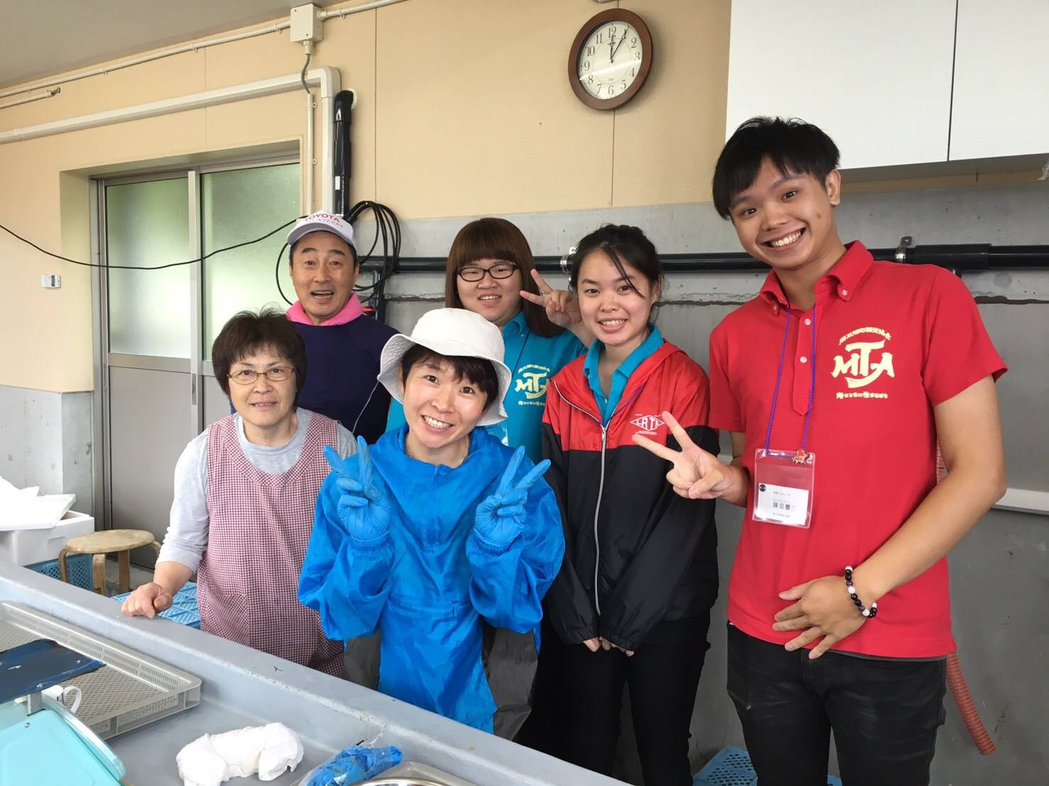 作業台のある室内で、地元の方3人と、留学生3人が並んで笑顔でピースサインをしている記念撮影の写真