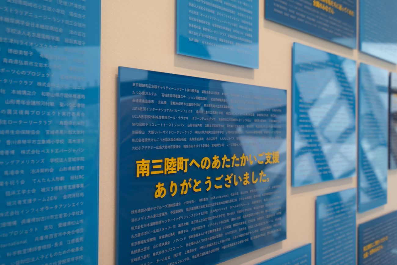 青いプレートには「南三陸町へのあたたかいご支援 ありがとうございました。」と大きく書かれ、多くの団体や個人の名前が記されている写真