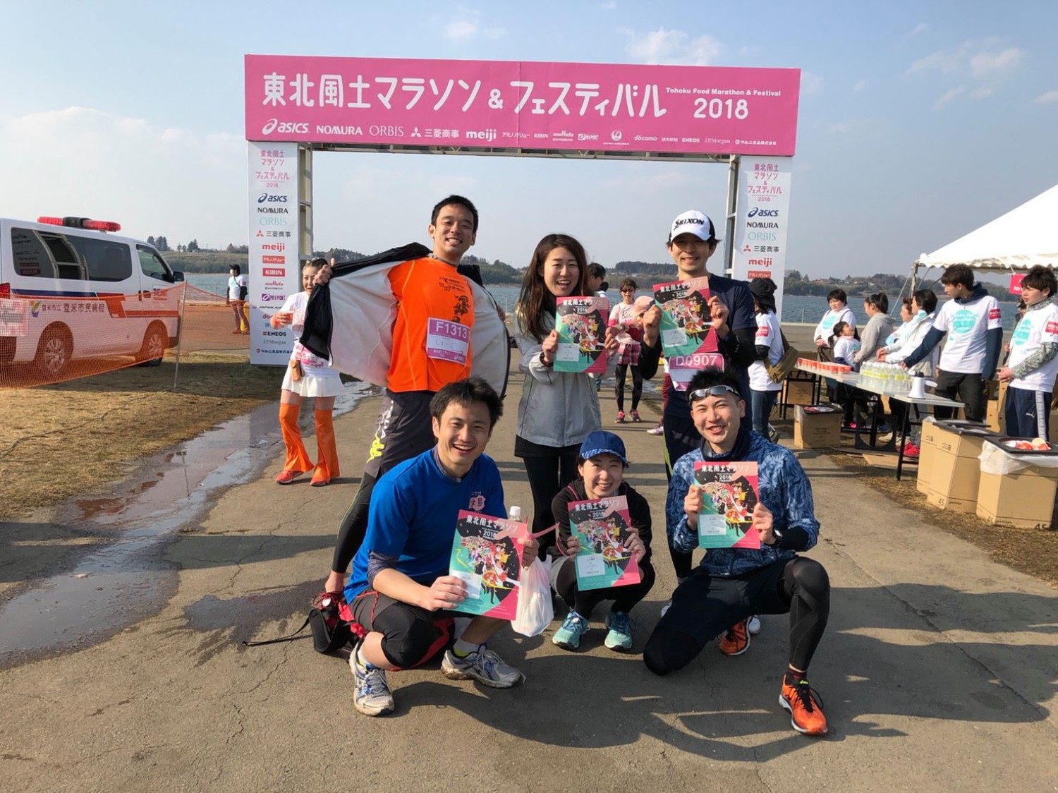 「東北風土マラソン＆フェスティバル2018」と書かれたゲートの前で、ゼッケンを付けた6人の男女が大会パンフレットを持って笑顔で記念撮影している写真