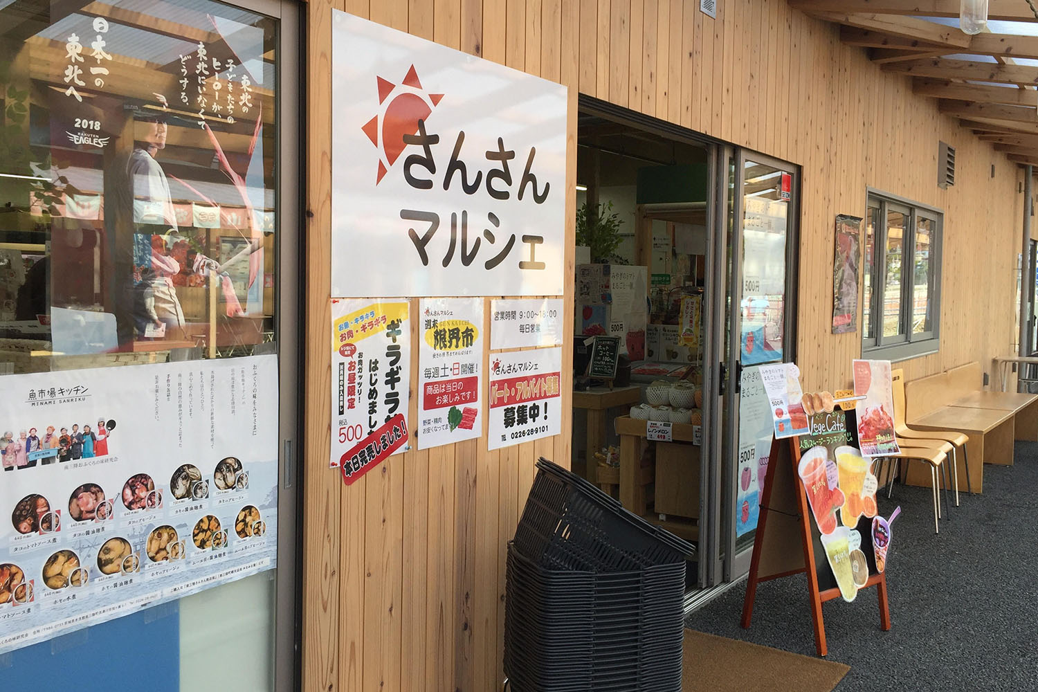 店内に商品が並び、様々なチラシや広告が貼られている木造の建物の入り口に「さんさんマルシェ」と書かれた白い看板が掲げられている写真