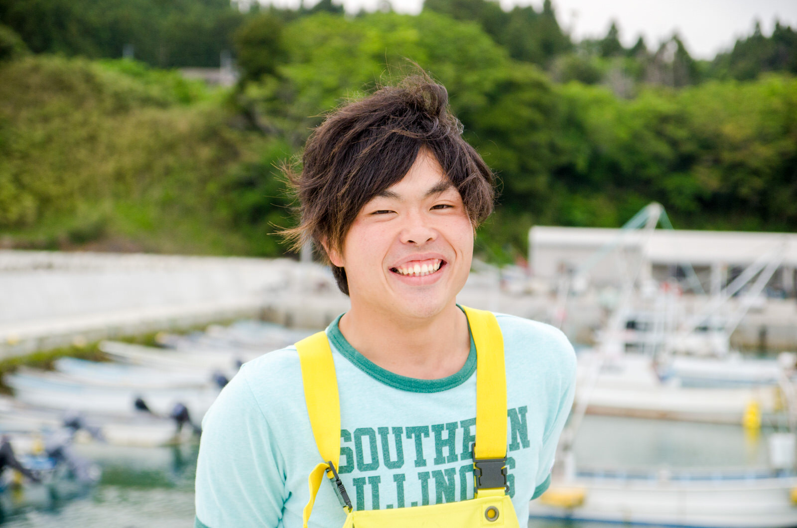 漁船と緑の山を背景に笑顔の浅野さんの写真