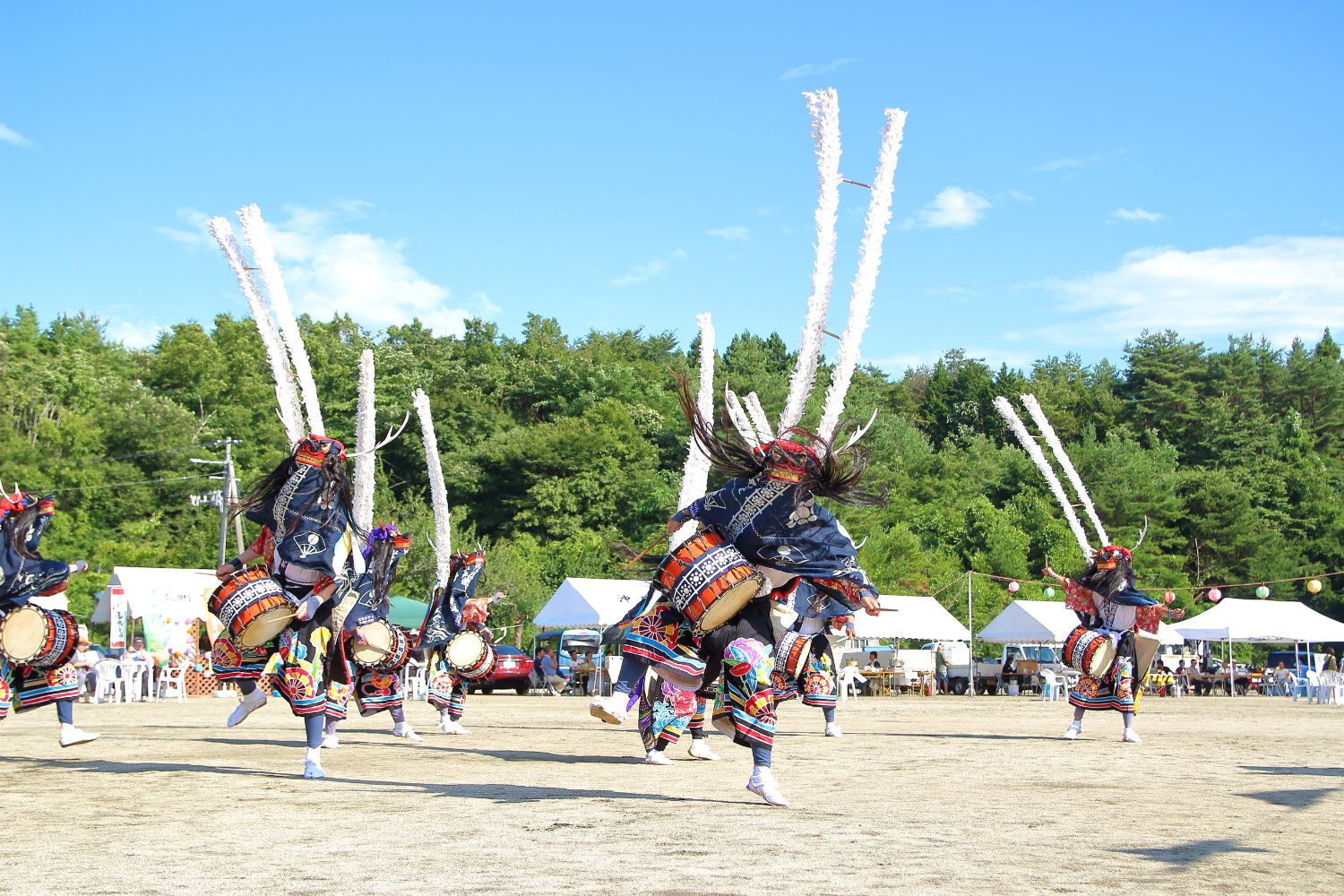 色鮮やかな衣装に身を包み、背中に太鼓を背負って踊る鹿踊りの踊り手たちが、躍動感あふれる動きで演舞を披露している写真