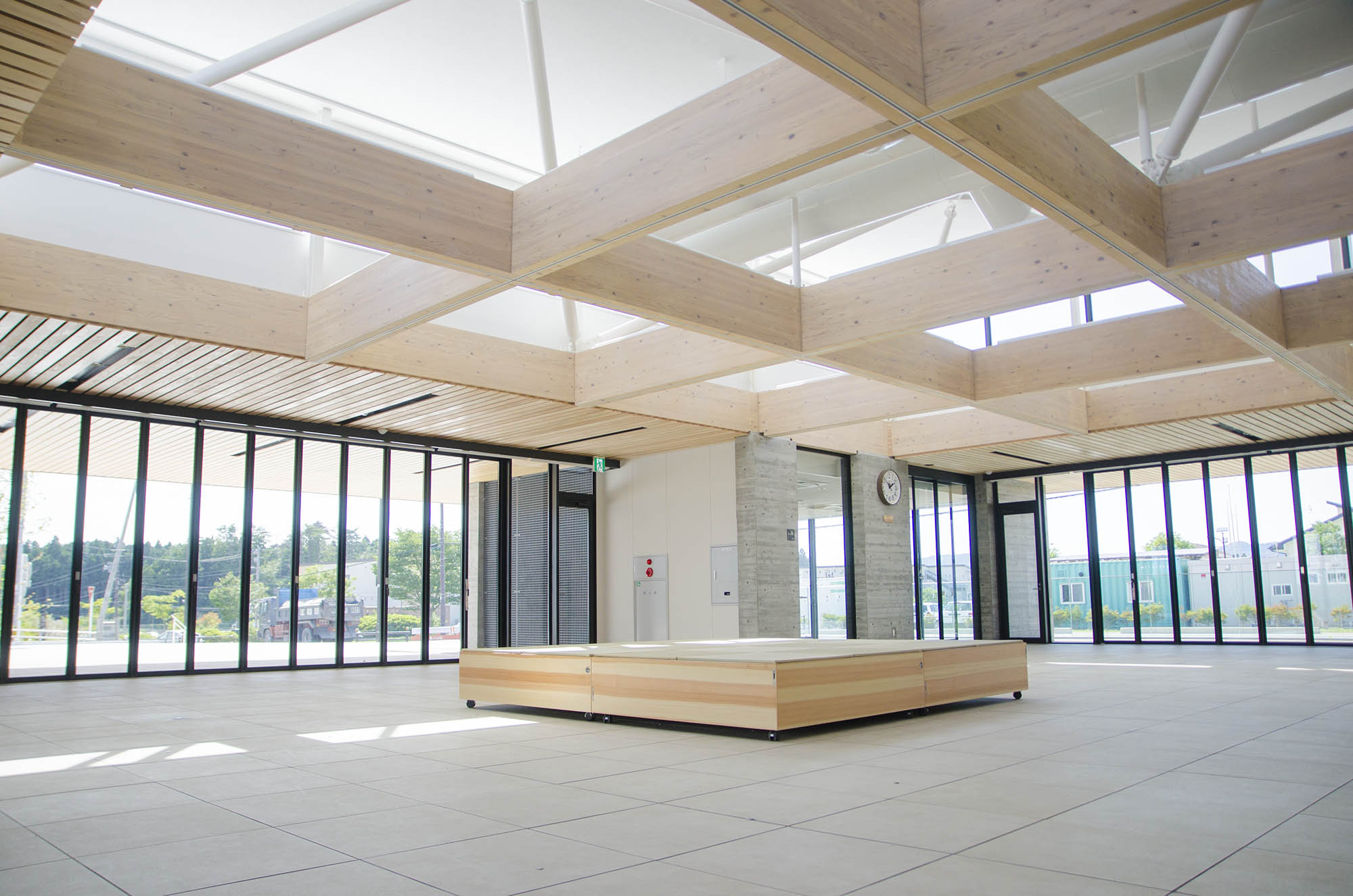 天井から自然光が差し込む明るく広々としたロビーに、木材を使った天井の格子と中央に置かれた木製のベンチがある南三陸町役場の新庁舎内部の写真