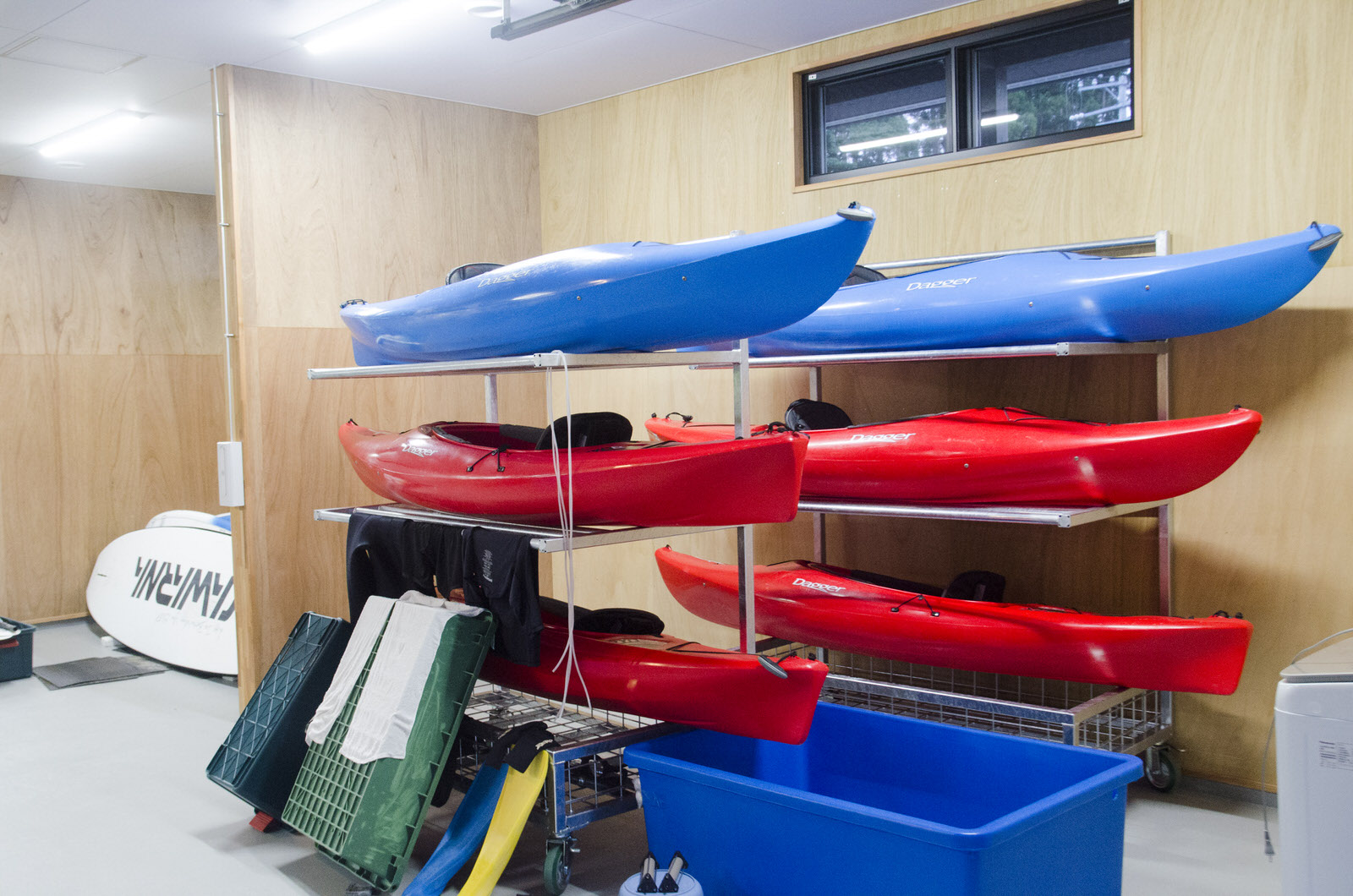 木の壁の室内に設置された2台の棚に、赤や青のカヤックが整理されて置かれている倉庫内の写真