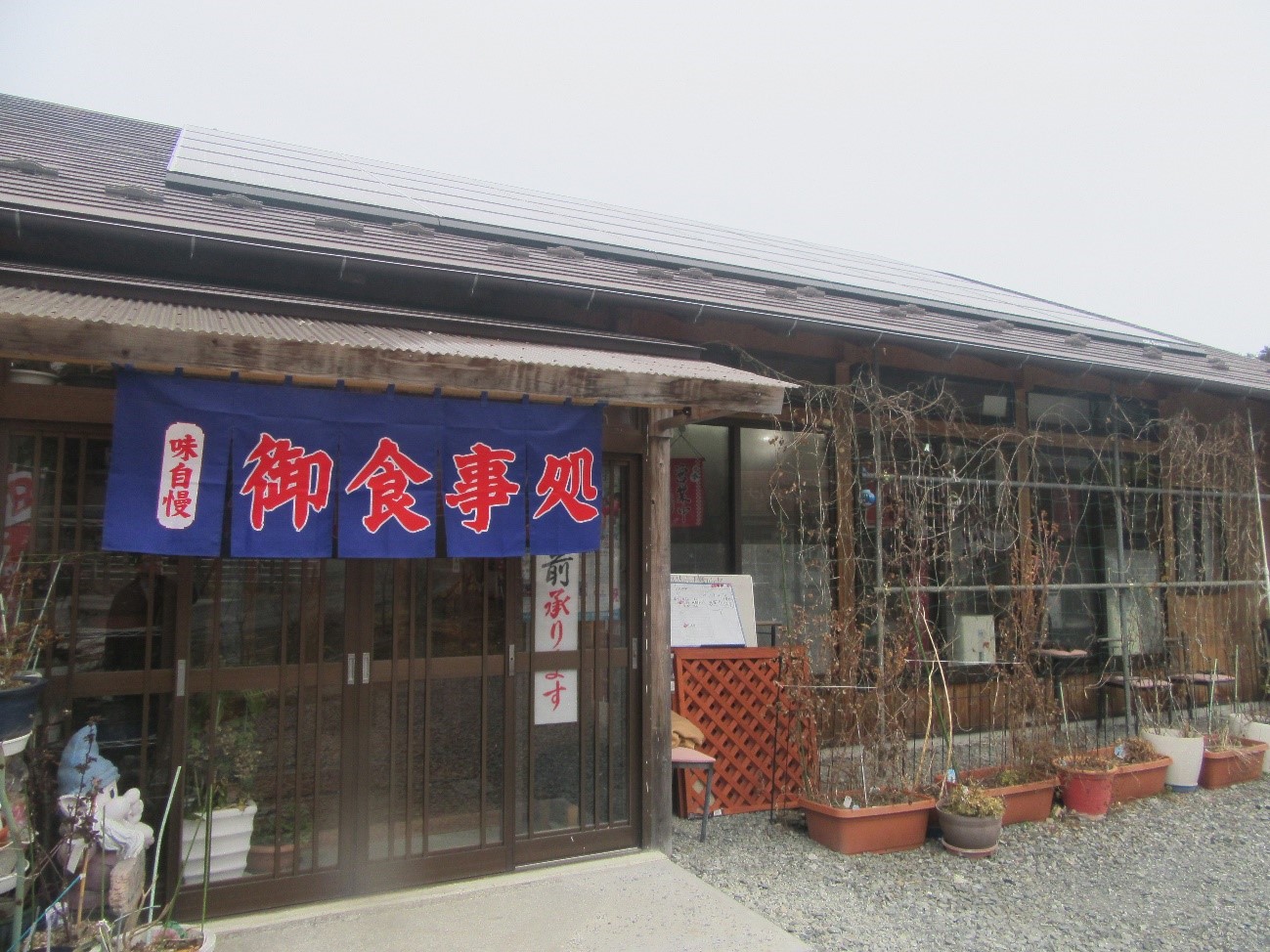 建物の入り口に、「御食事処」と赤い文字で書かれた青い暖簾が掛かっているレストラン入り口の写真