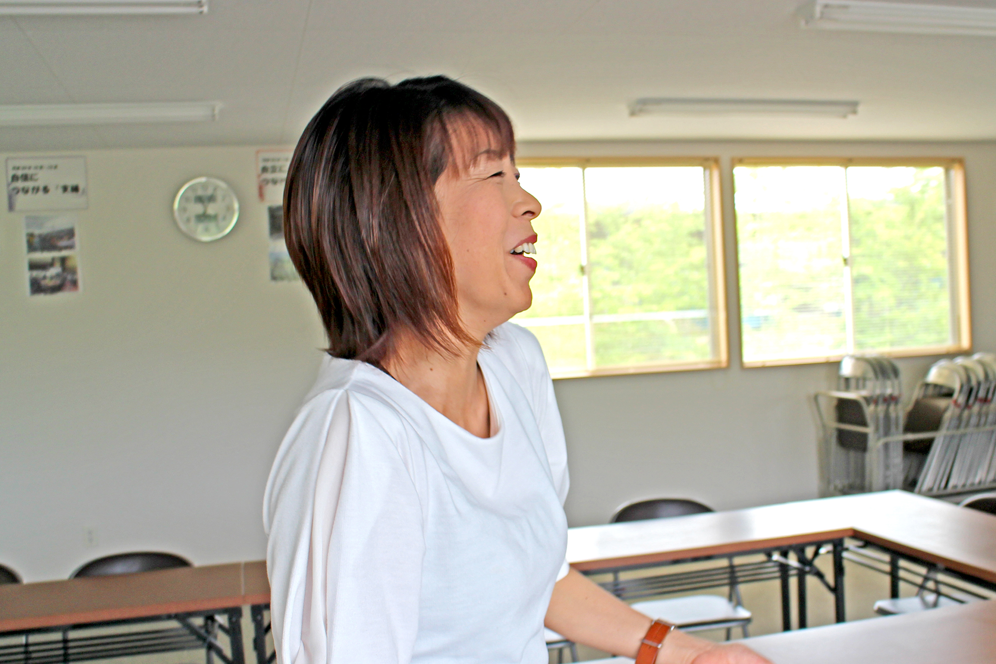 長机と椅子が並んだ室内で高橋さんが横を向いて笑顔を見せている写真