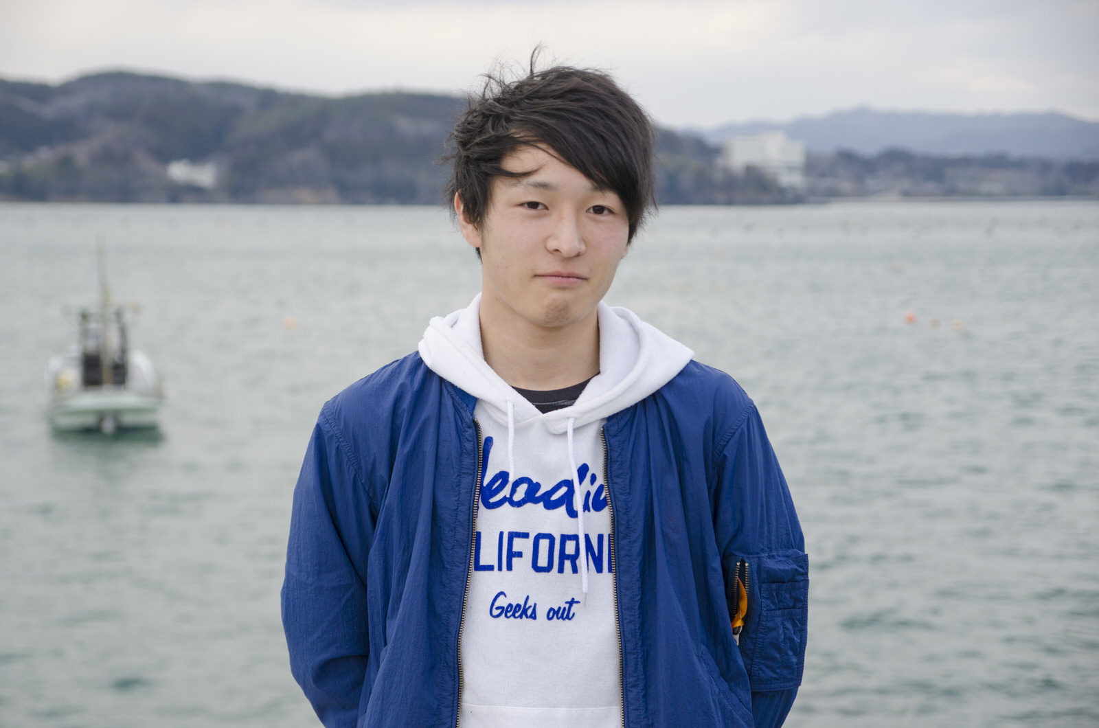 青いジャケットを着た小野寺さんが海を背景にカメラを見つめている写真