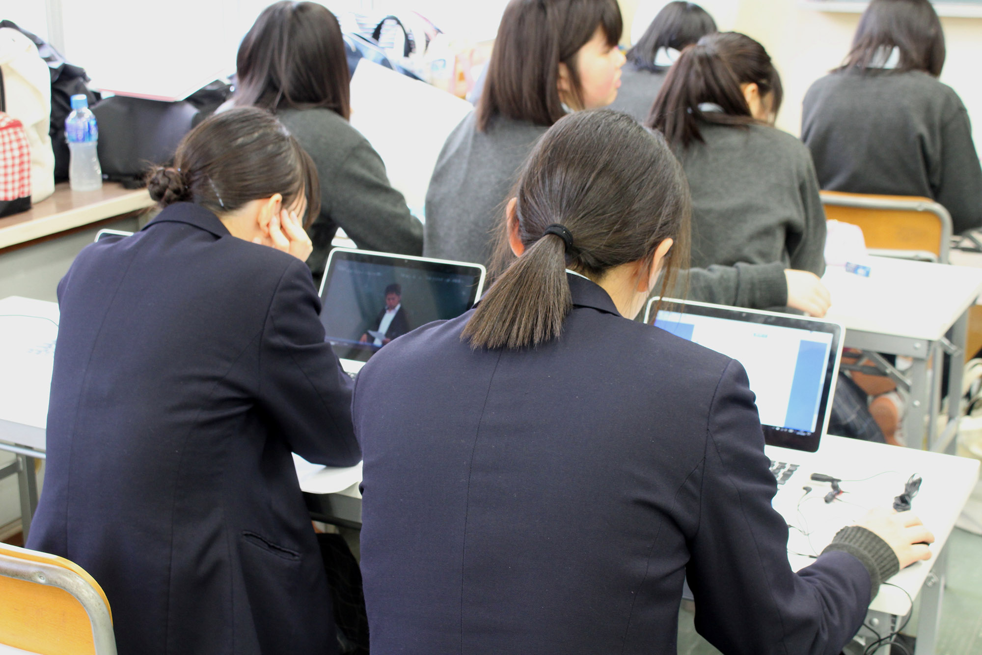 教室内に並べられた机に座りタブレットを使ってICT学習に取り組んでいる2人の女子生徒の姿を後方から撮影した写真