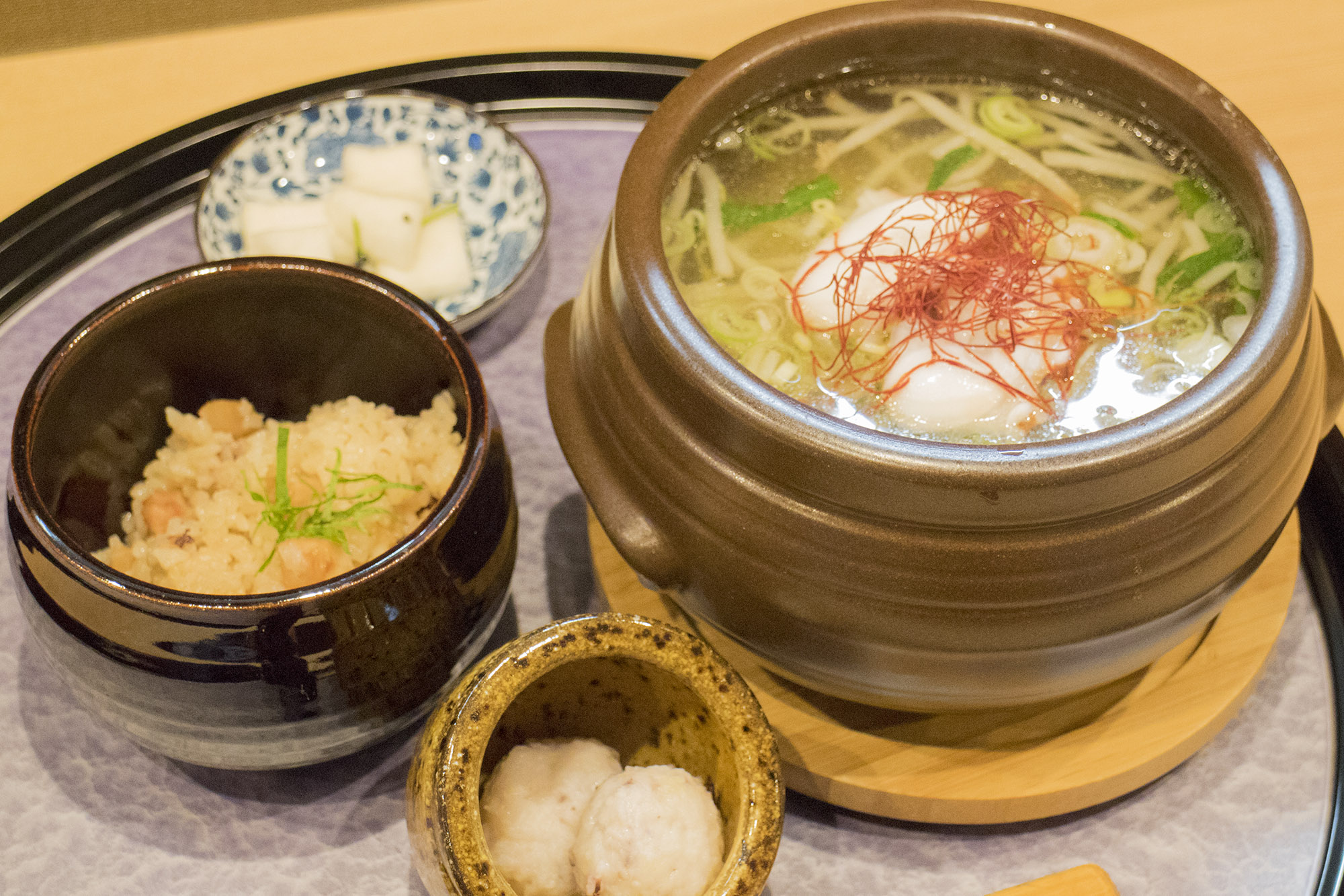 丸いお盆の上に、タコつぼ風の土鍋に入ったラーメン、タコ飯、2つの小皿が載っている写真