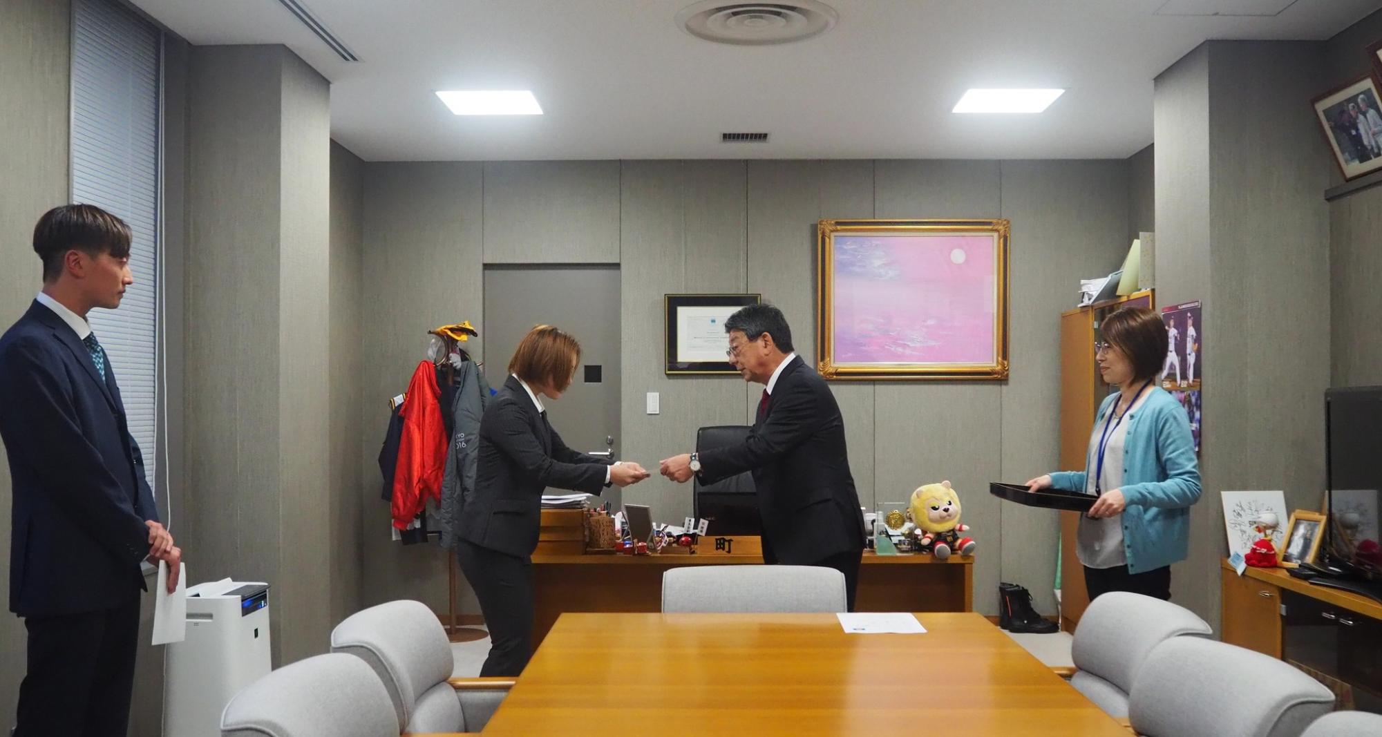 周囲には他の職員が立ち会っており、渡邉さんが男性から丁寧に書類を受取る様子の写真