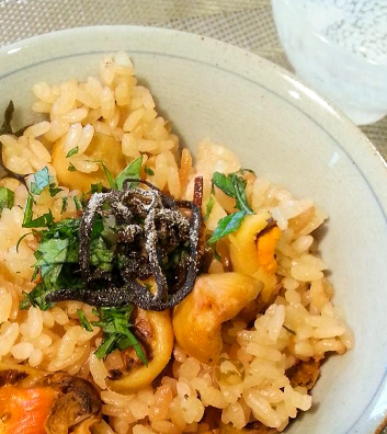 茶碗に盛り付けられた、ホヤの身がたくさん入り、大葉と塩昆布が添えられたホヤの炊き込みご飯の写真