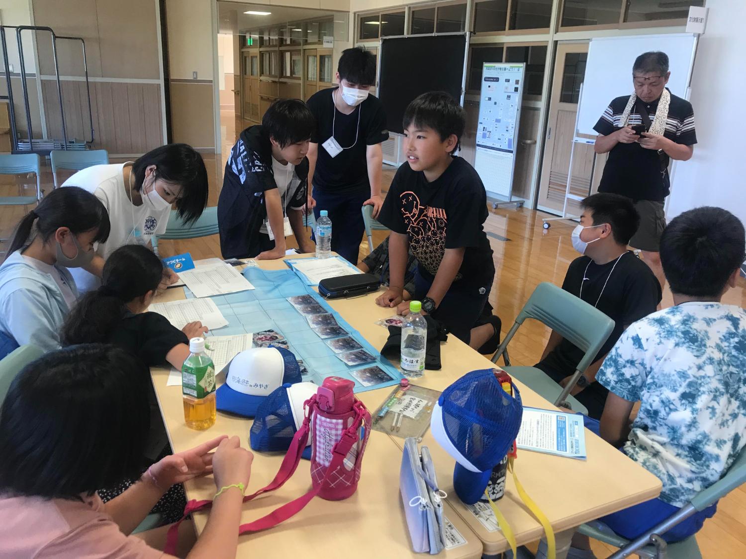 子どもたちと高校生が円卓を囲んで資料を見ながら、ボードゲームを楽しんでいる様子の写真