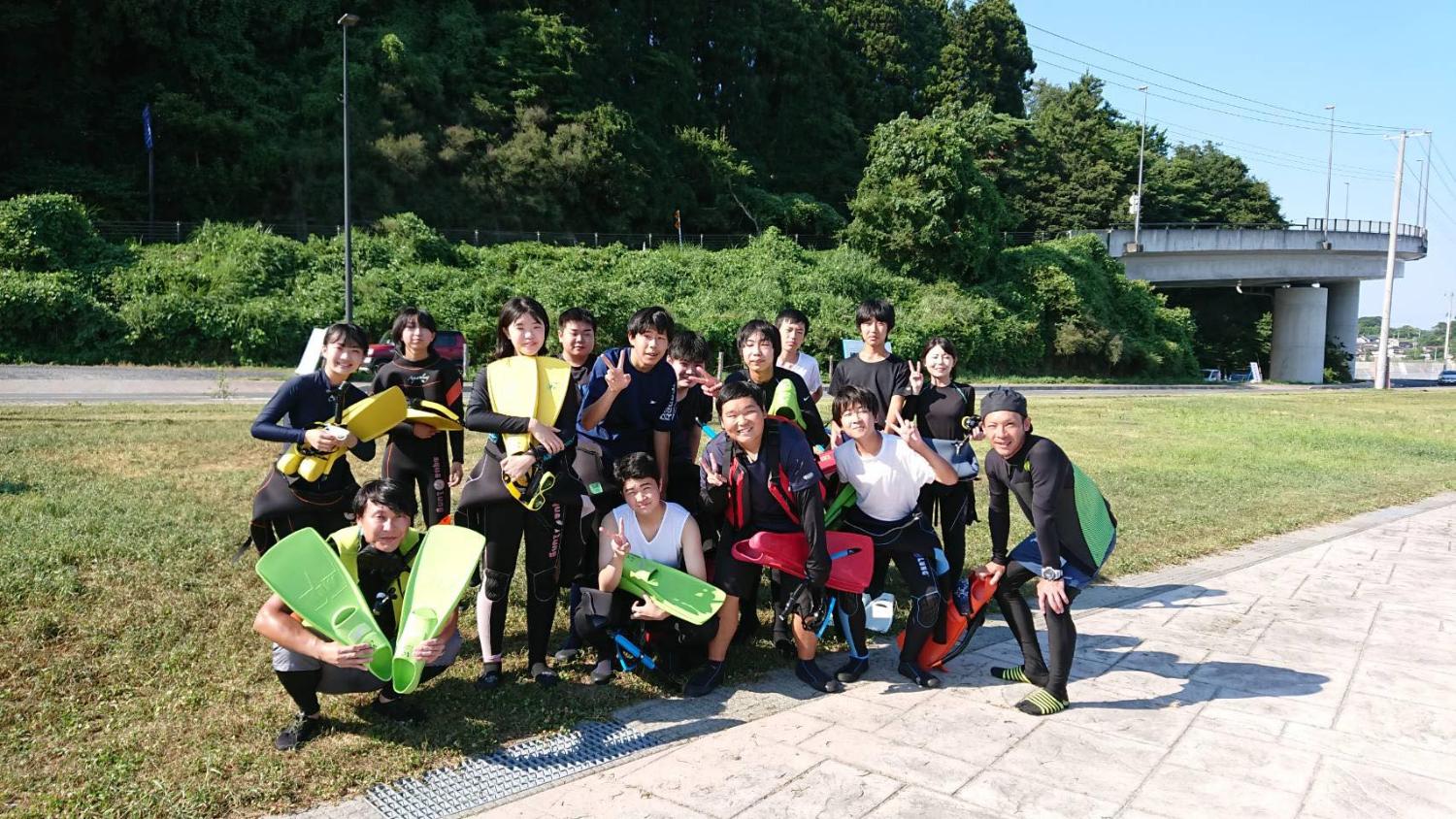 南三陸高校の生徒たちがウェットスーツとフィンを装着して海辺に集合し、笑顔でポーズをとっている写真