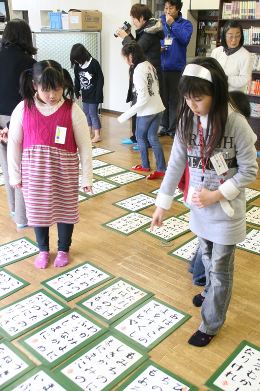 床の上に大きな百人一首の札がたくさん並べられ、参加した子どもたちが、札を指さしながら、お目当ての札を探している様子の写真