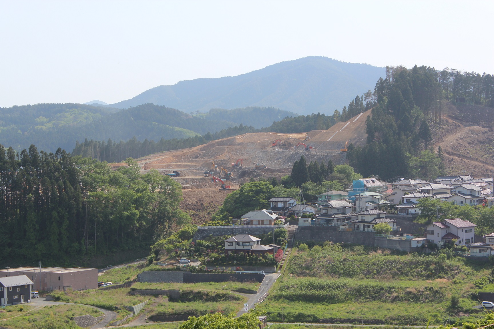 複数の重機が稼働中で、住宅街と山の境界が明確に分かる写真