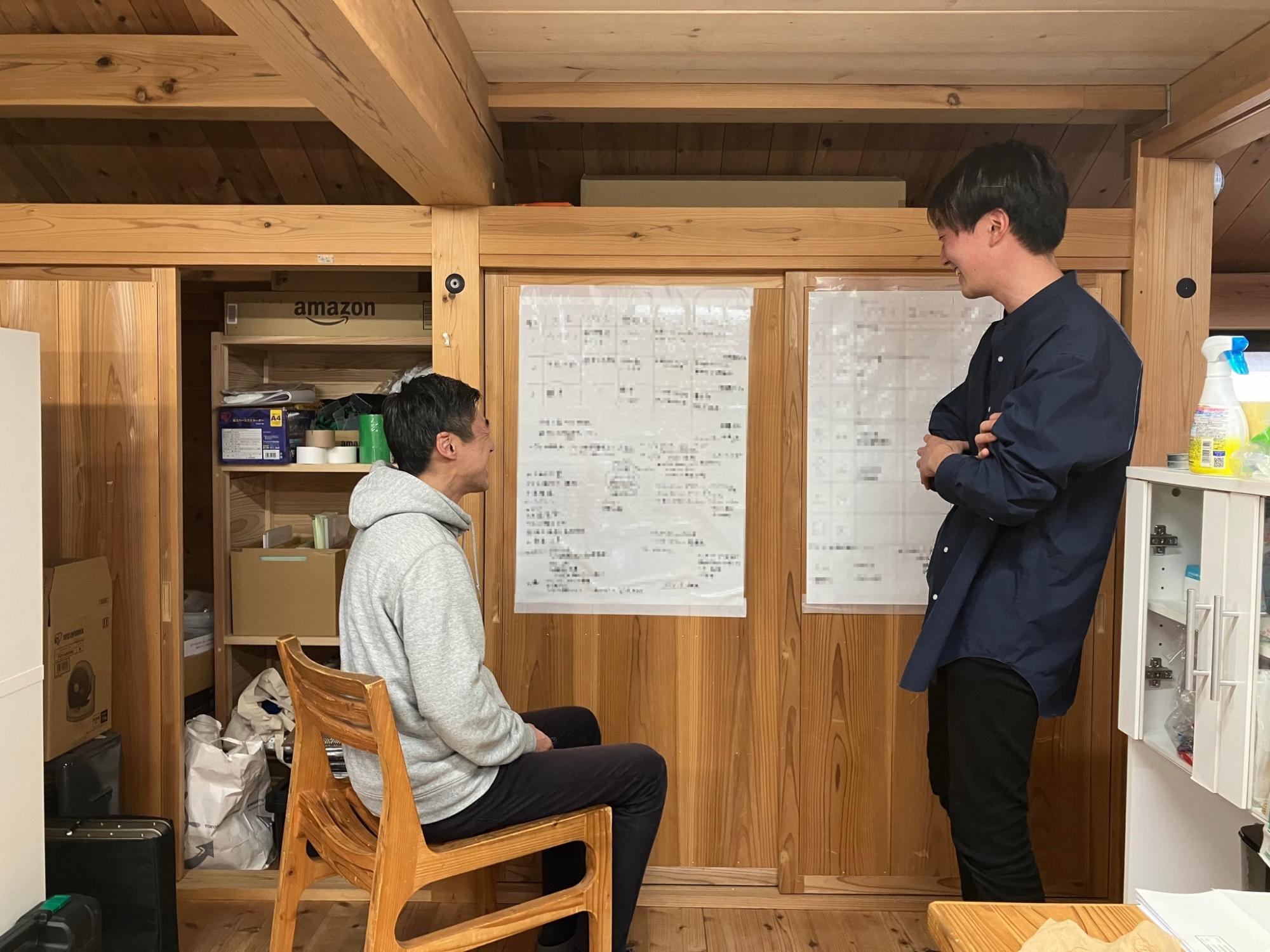 木造の部屋の中で、星空之介さんと男性がホワイトボードに書かれた内容を見ながら話し合っている写真