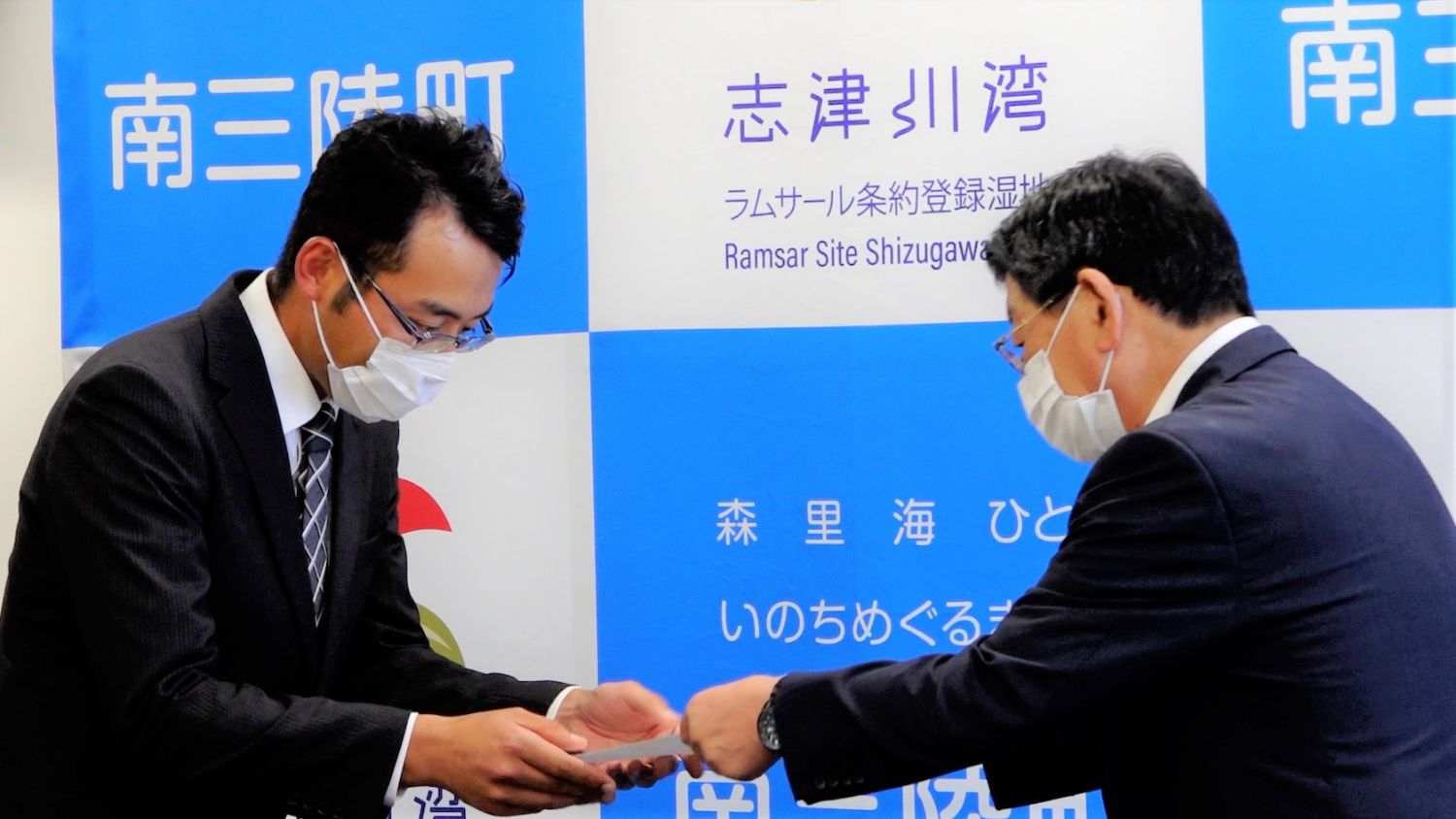 南三陸町役場の庁舎内で、スーツ姿の佐藤仁町長から委嘱状を受け取る太田さんの写真