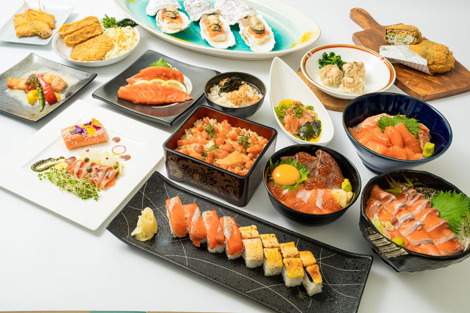 テーブルの上にさまざまな種類のサーモンを使った刺身や寿司、焼き物、揚げ物、蒸し物などが複数の皿に盛り付けられて並べられている様子の写真