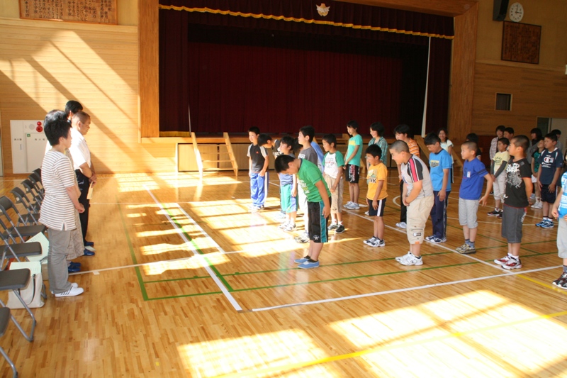 体育館で、入谷打囃子の練習開始にあたり、整列した子どもたちが講師の方々に向かって一斉に頭を下げて挨拶をしている様子を写した写真