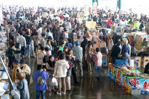 屋内の広い会場に非常に多くの人々が密集し、その中でフリマや露店のような商品の並んだブースが展開されている様子を捉えた南三陸町産業フェアの様子の写真