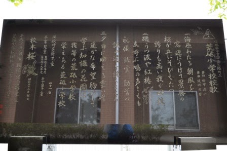 二つの窓が反射する黒い石碑に、校歌の歌詞と「荒砥小学校校歌」の文字が刻まれている写真