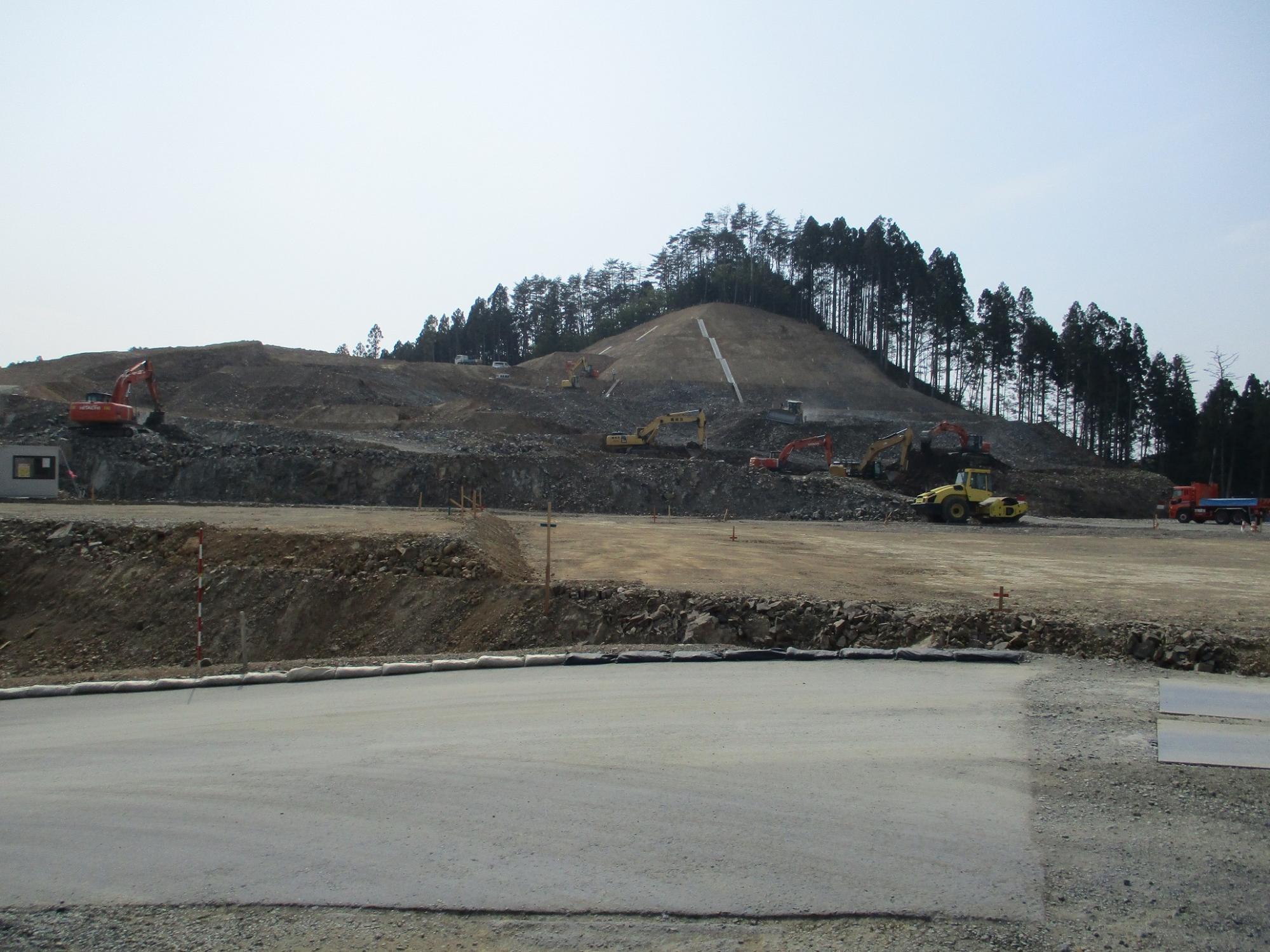山の斜面が大規模に削られ、複数のショベルカーやダンプカーが稼働している造成工事現場の様子を広く写した写真