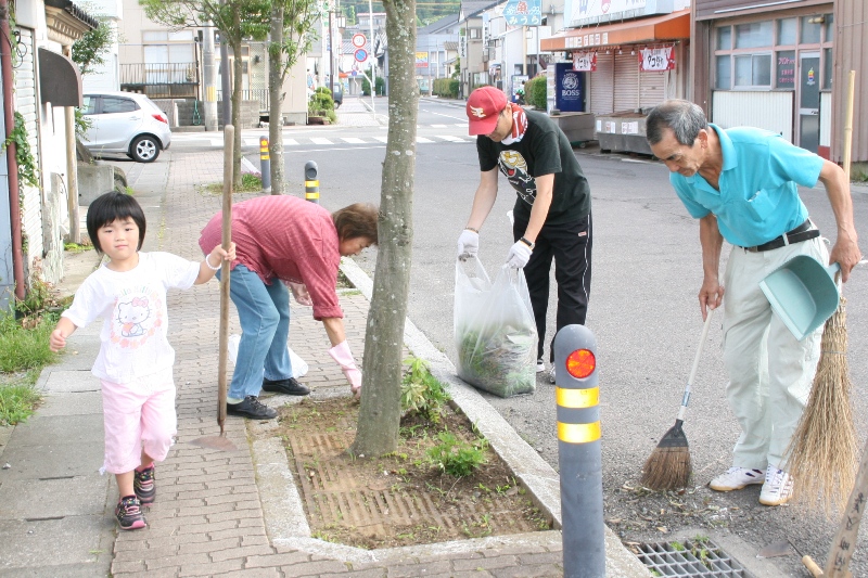 大人3人と子ども1人がほうきやちりとり、ゴミ袋を使って清掃活動を行い、雑草やゴミを集めているリアスクリーン作戦の様子を写した写真